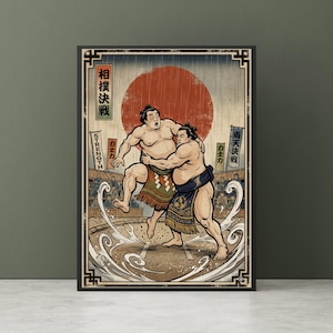 May include: Framed print of a sumo wrestling scene. Two wrestlers grapple, set against a red sun and Japanese text. The artwork uses bold lines and a vintage style, emphasising strength and competition. The print is framed in a black border.