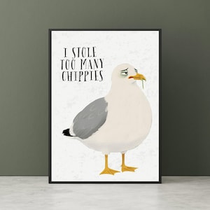 May include: A framed print featuring a cartoon seagull with a guilty expression, a green item in its beak, and the text "I STOLE TOO MANY CHIPPIES" in black. The seagull has white and gray feathers and yellow feet.