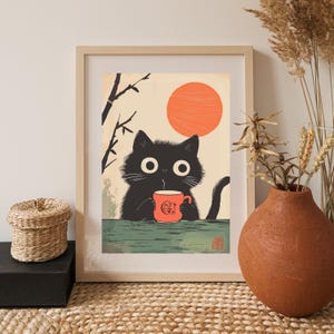 May include: Framed art print featuring a black cat holding an orange mug with Japanese text. The cat has large white eyes and is set against a backdrop of a rising orange sun and bamboo. The print is in a wooden frame.