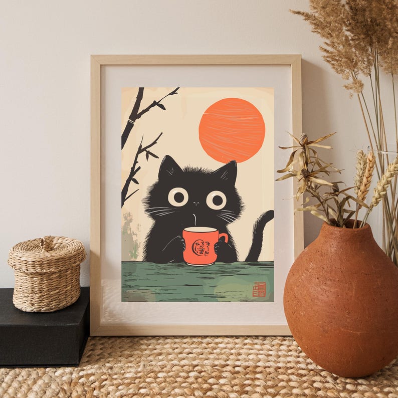 May include: Framed art print featuring a black cat holding an orange mug with Japanese text. The cat has large white eyes and is set against a backdrop of a rising orange sun and bamboo. The print is in a wooden frame.