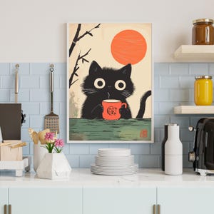 May include: A framed art print featuring a black cat holding a red mug with a graphic design. The cat is set against a backdrop of a rising orange sun and a minimalist landscape. The print is displayed in a kitchen setting.