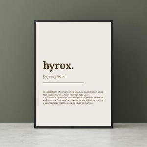 May include: A framed print with the word "hyrox" in a bold, dark font. Below, the definition of "hyrox" is provided, describing it as a specialized endurance race. The background is a light beige color.