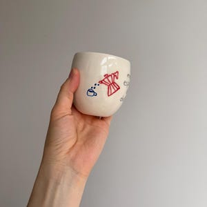 May include: White ceramic mug with a red and blue illustration of a coffee pot pouring coffee into a cup. The text "My espresso dreams" is written on the mug.