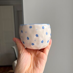 Puede incluir: Un peque&ntilde;o cuenco de cer&aacute;mica blanca con un patr&oacute;n floral azul. El cuenco tiene una superficie ligeramente texturizada y una forma redondeada.