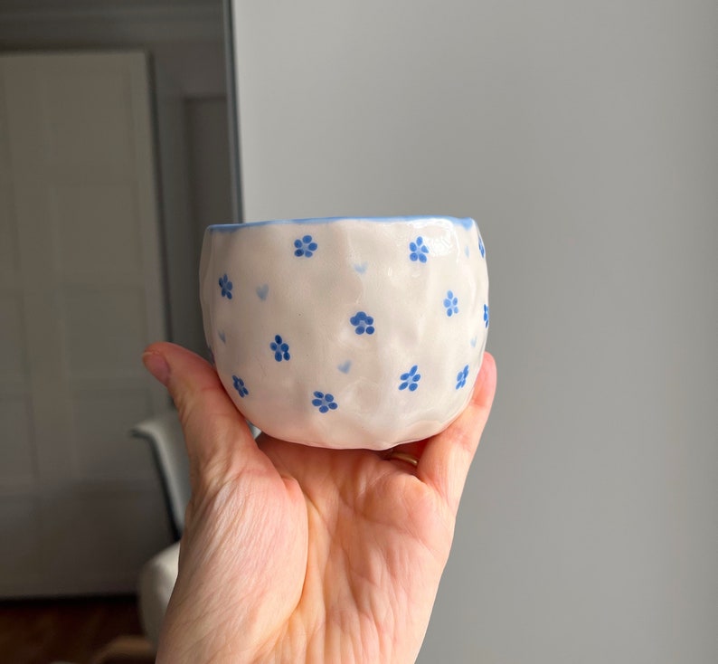 Puede incluir: Un peque&ntilde;o cuenco de cer&aacute;mica blanca con un patr&oacute;n floral azul. El cuenco tiene una superficie ligeramente texturizada y una forma redondeada.