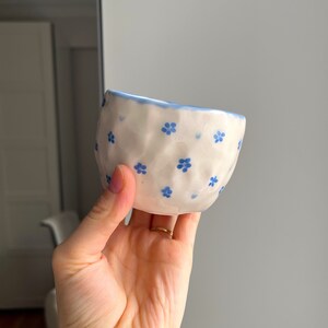 Puede incluir: Un peque&ntilde;o cuenco de cer&aacute;mica blanca con un patr&oacute;n floral azul. El cuenco tiene una superficie texturizada, ligeramente abultada.