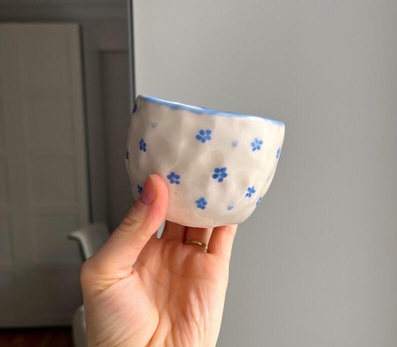 Puede incluir: Un peque&ntilde;o cuenco de cer&aacute;mica blanca con un patr&oacute;n floral azul. El cuenco tiene una superficie texturizada, ligeramente abultada.