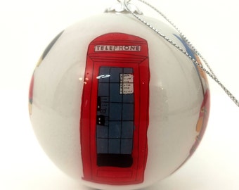 May include: White Christmas ornament with a red telephone booth illustration. The booth has a blue door and the word "TELEPHONE" is printed in black above the door.
