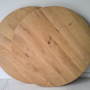 Op de afbeelding: Twee ronde tafelbladen van lichtbruin hout. Het hout heeft zichtbare nerven en knopen. Het ronde ontwerp is geschikt voor een eettafel of decoratief gebruik. Elk blad heeft een diameter van ongeveer 76 cm.