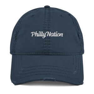 Puede incluir: Una gorra de béisbol azul oscuro desgastada con el texto "Philly Nation" bordado en blanco en la parte delantera.
