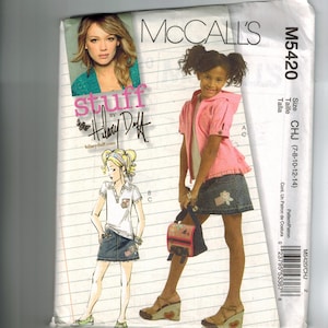May include: McCall's sewing pattern featuring a design by Hilary Duff. The pattern includes illustrations of girls' clothing, including a pink hooded jacket, denim skirt, and a white polo shirt. The pattern size is CHJ (7-8-10-12-14).