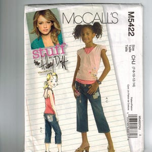 May include: A sewing pattern for a girl's cropped jeans with a floral design. The pattern is from McCall's and is called "Stuff by Hilary Duff".
