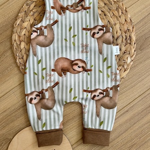Könnte beinhalten: Baby-Strampler mit hellgrünem und weißem Streifenmuster, mit braunen Faultieren, die an Ästen hängen. Der Strampler hat braune Bündchen und den Text "Take it slow".