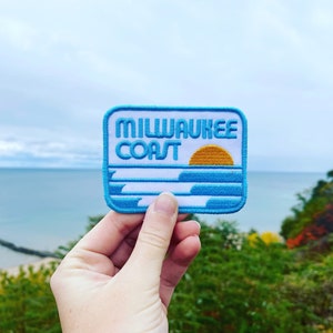 May include: A blue and white embroidered patch with the text "Milwaukee Coast" and a yellow sun setting over blue waves.