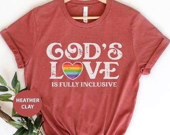 May include: A heather clay t-shirt with the text "God's Love is Fully Inclusive" in white with a rainbow heart.