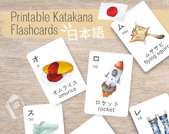 May include: Printable flashcards featuring Japanese Katakana characters with illustrations. The cards include images of a rocket, sneakers, a flying squirrel, a plate of omurice, peanuts, and rain boots.