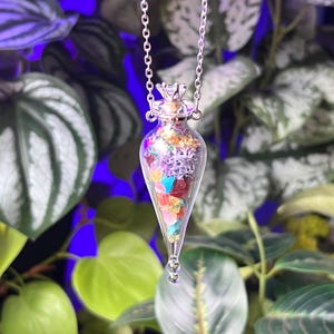 May include: A silver chain necklace with a clear glass pendant shaped like a teardrop. The pendant is filled with colorful crystals and topped with a silver crown.