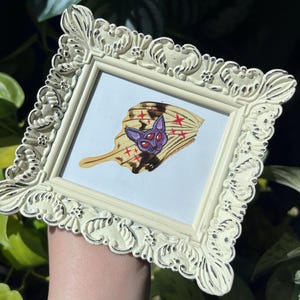 May include: A framed illustration of a butterfly with a cat's face and red stars on its wings.