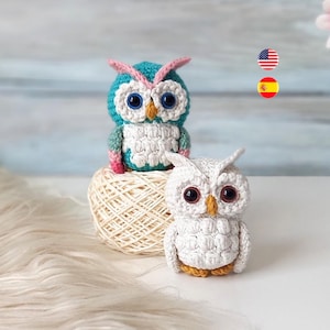 May include: Two handmade crochet owls. One is teal, white, and pink, the other is white with brown eyes. They sit on a ball of yarn. The owls have large, round eyes and are made with detailed stitching.