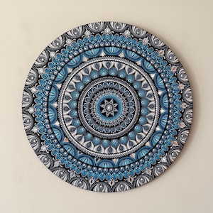 May include: A circular wall art piece featuring a detailed mandala design. The artwork is composed of concentric rings of dots in shades of blue, white, silver, and black, creating a symmetrical pattern that radiates from a central silver star.