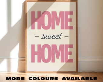 Puede incluir: Una impresión enmarcada con el texto "HOME - sweet - HOME" en letras rosas sobre un fondo crema. El marco es de madera clara.