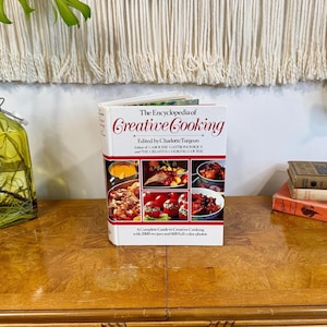 May include: The Encyclopedia of Creative Cooking, edited by Charlotte Turgeon, is a hardcover cookbook featuring a white cover with red text and a grid of six color photographs displaying various prepared food dishes on the front cover.