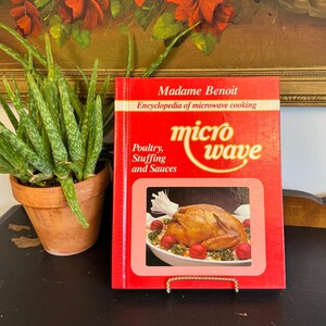 May include: A red hardcover cookbook titled Madame Benoit Encyclopedia of microwave cooking, with the subtitle Poultry, Stuffing and Sauces. The cover features a central rectangular photograph of a roasted chicken on a white platter.