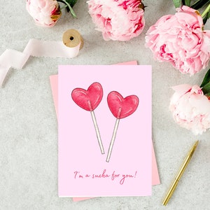 Op de afbeelding: Een roze kaart met twee rode hartvormige lolly's en de tekst "Ik ben gek op je!"