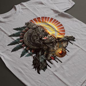 May include: White t-shirt featuring a detailed graphic of an Aztec warrior with a feathered headdress, set against a sunburst design. The warrior has face paint and ornate armor. The design incorporates shades of brown, red, and gold.