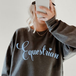 May include: A dark gray sweatshirt with the word "Equestrian" in light blue lettering with a small blue heart.