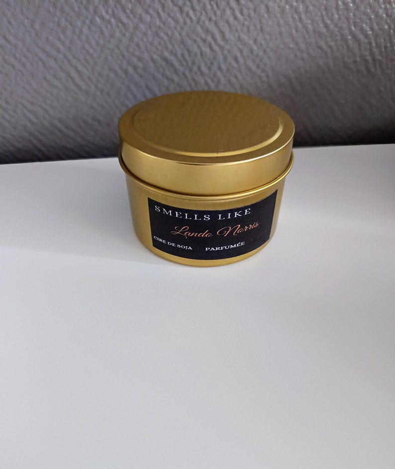Puede incluir: Un tarro de vela dorado con una etiqueta negra que dice "Smells Like Lando Norris" y "Cire de Soja Parfum&eacute;e".