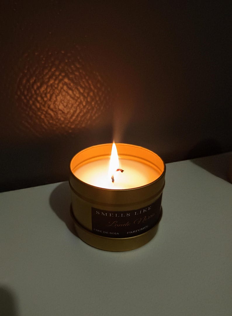 Puede incluir: Un tarro de vela dorado con una vela de cera de soja blanca en su interior. La vela est&aacute; encendida y la llama es visible. La etiqueta del tarro dice "Smells Like" y "Lumberjack" en una fuente cursiva. Tambi&eacute;n se puede ver el texto "Cire de Soja" y "Parfum&eacute;e" en la etiqueta.