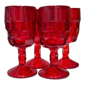 May include: A set of four matching red glass goblets featuring a faceted, geometric texture on the bowls and stems. Each goblet has a wide circular base, a thick textured stem, and a cylindrical bowl with a repeating hexagonal pattern.