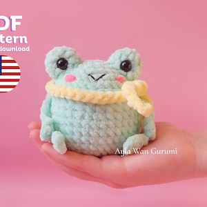 May include: A crochet pattern for a green frog wearing a yellow scarf. The pattern is available as an instant download. The image shows a crocheted frog toy.