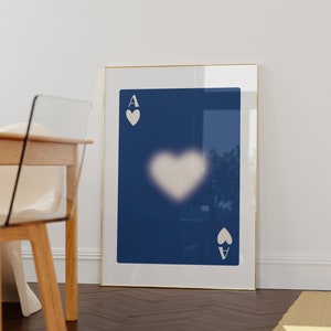May include: A framed print of an ace of spades playing card with a white heart shape in the center. The background of the card is a dark blue color.