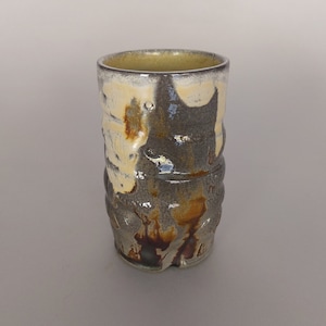 May include: A ceramic mug with a textured, brown, yellow, and white glaze. The mug has a cylindrical shape and a slightly flared rim.