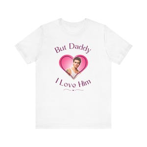 May include: White t-shirt with a pink heart graphic featuring a man's face. The text "But Daddy I Love Him" is printed below the heart.