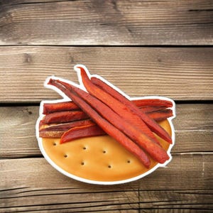 May include: A sticker featuring a cartoon depiction of a cracker topped with strips of red meat. The cracker is tan with small holes, and the meat is a deep red color. The sticker is set against a wooden background.