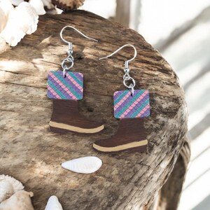 May include: A pair of wooden earrings shaped like boots with a pink, purple, and green mermaid scale pattern on the top of each boot.