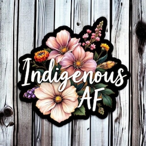 Könnte beinhalten: Aufkleber mit floralem Design und dem Text "Indigenous AF". Die Blumen sind in Rosa-, Orange- und Gelbtönen gehalten, mit grünen Blättern, vor einem schwarzen Rand und einem Holzgrund.