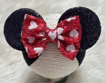 May include: Red and white sequin bow with black fabric mouse ears. The bow has white hearts on a red background. The ears are black with sequins.