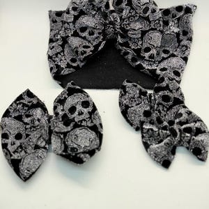 May include: A set of three black velvet hair bows with a silver glitter skull pattern. The bows are in different sizes and are perfect for adding a touch of spooky style to any outfit.