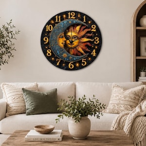 May include: A round wall clock featuring a celestial design with a sun and moon. The clock face is black with gold numerals and a detailed illustration of the sun and moon. The clock is mounted on a cream-colored wall above a beige sofa.