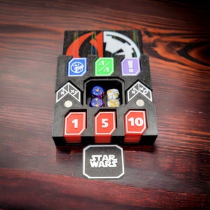 May include: A black plastic dice tray with compartments for different dice sizes. The tray has a Star Wars logo on the front and includes a set of dice.