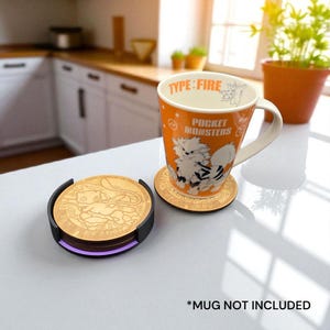Könnte beinhalten: Eine orangefarbene Tasse mit weißem Henkel und ein passender Untersetzer mit Pokémon-Design. Auf der Tasse steht "TYPE: FIRE" und "POCKET MONSTERS". Ein Stapel Untersetzer mit schwarzem Halter ist ebenfalls zu sehen.