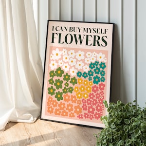 Può includere: Una stampa incorniciata con uno sfondo rosa e il testo "Posso comprarmi dei fiori" in lettere nere. La stampa presenta un motivo colorato di fiori in verde, blu, giallo e rosa.