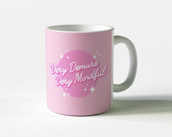 May include: A pink ceramic mug with a white handle. The mug has a pink circle with the text "Very Demure Very Mindful" in white.