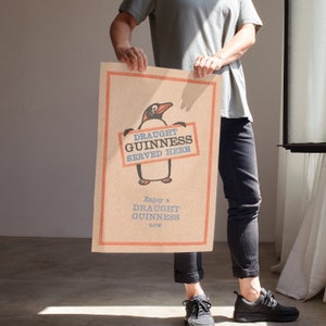 Puede incluir: Un p&oacute;ster de estilo vintage con un ping&uuml;ino de dibujos animados sosteniendo un cartel que dice "Draught Guinness Served Here". El p&oacute;ster tiene un fondo marr&oacute;n con acentos rojos y azules. El texto "Enjoy a Draught Guinness now" est&aacute; impreso debajo del ping&uuml;ino.