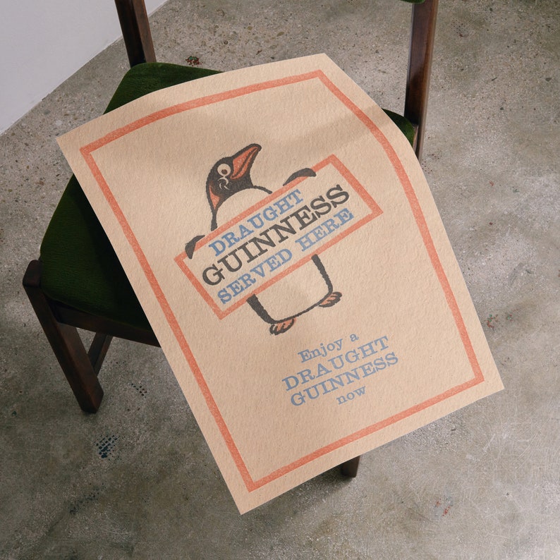 Puede incluir: Un cartel marr&oacute;n y naranja con un ping&uuml;ino de dibujos animados sosteniendo un cartel que dice "Draught Guinness Served Here". El cartel tambi&eacute;n dice "Enjoy a Draught Guinness now".