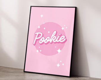 May include: Pink framed print with a pink circle and white text that says "Pookie" with white stars around the circle.